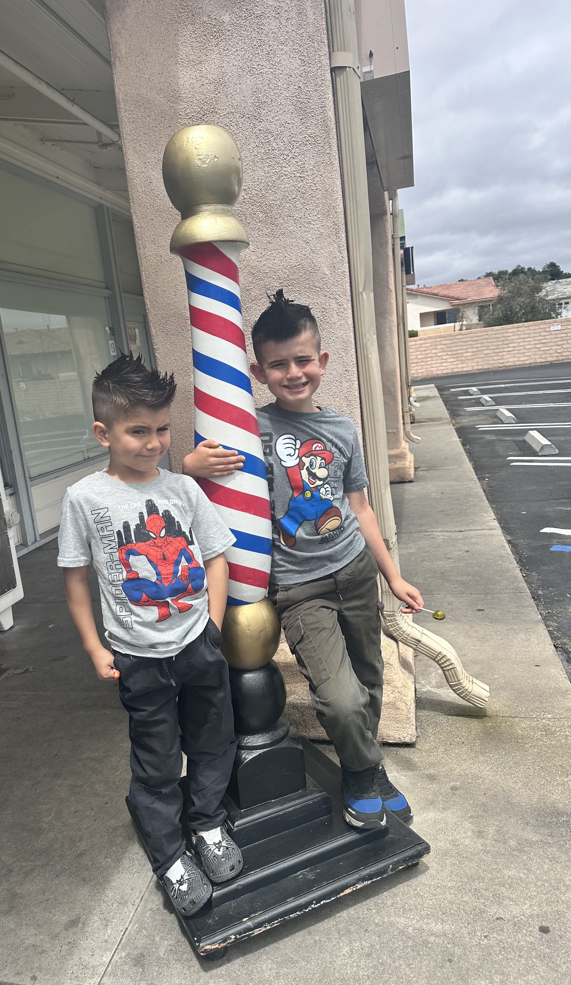 Two young customers posing with the shop's barber pole